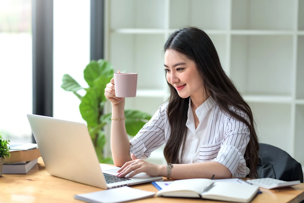 Beautiful young Asian businesswoman drinking a coffee working on laptop at office.