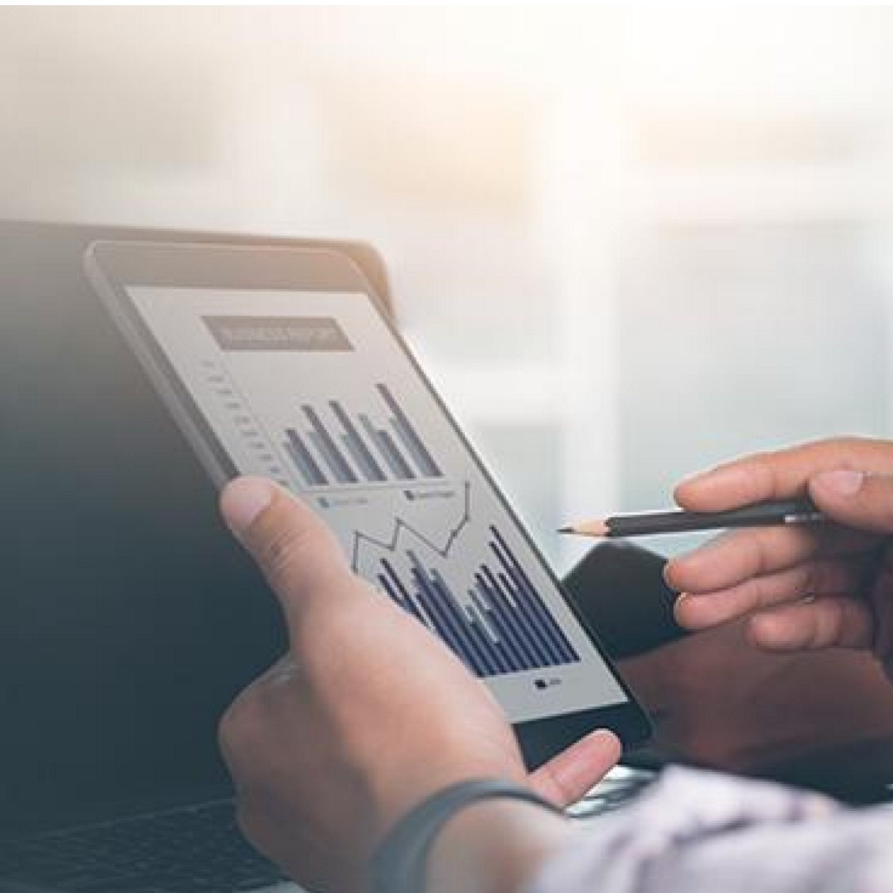 A man looking at a graph on his tablet while holding a pencil.