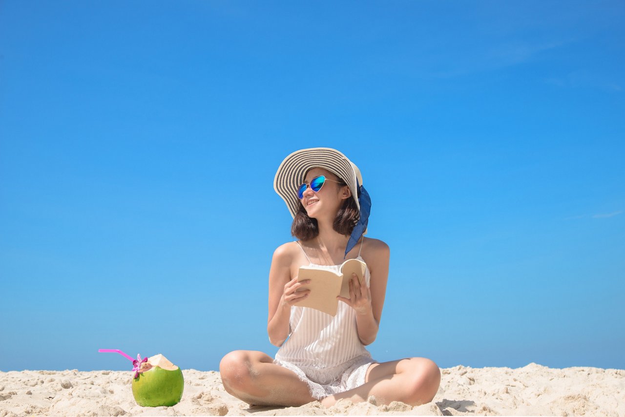 young woman enjoy smile reading a book on the sea beach with drinking fresh coconut, background with cleared sky blue