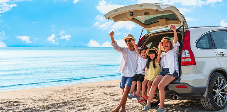 A family as they enjoy the beach, sitting on the open trunk of their SUV