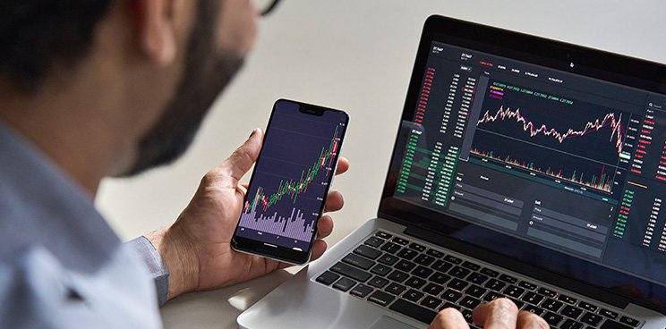 A man looking at graphs on a laptop and mobile phone.