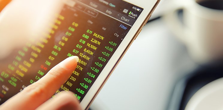 A hand scrolling through a tablet screen that shows investment figures.