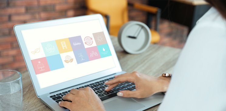 A laptop on a table with a clock beside it and its monitor showing a collage of icons and logos.