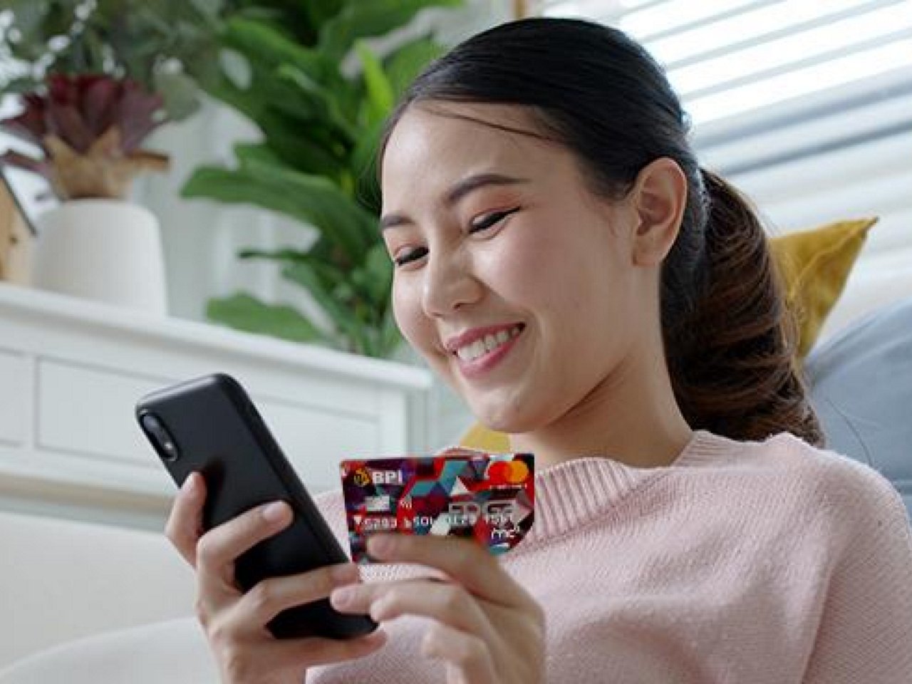 A smiling woman holding her phone and card.