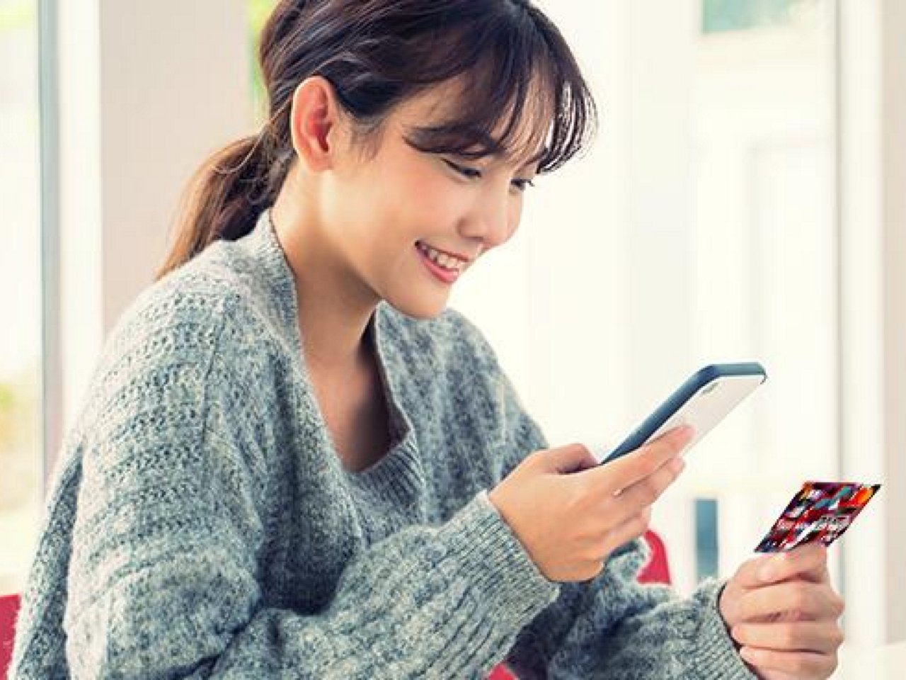 A smiling woman holding her phone and card.