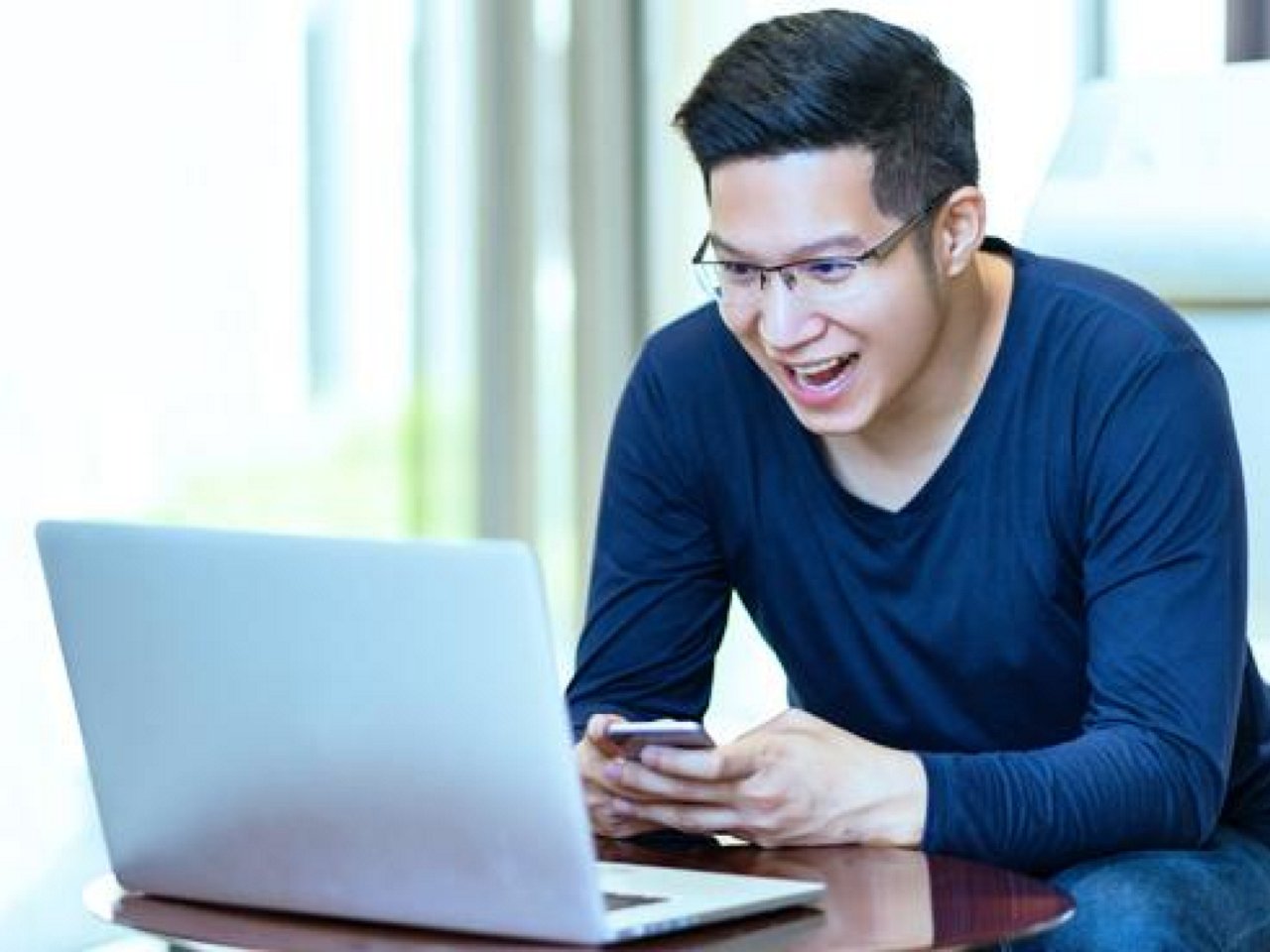 A man looking amazed as he works on his mobile phone  and laptop