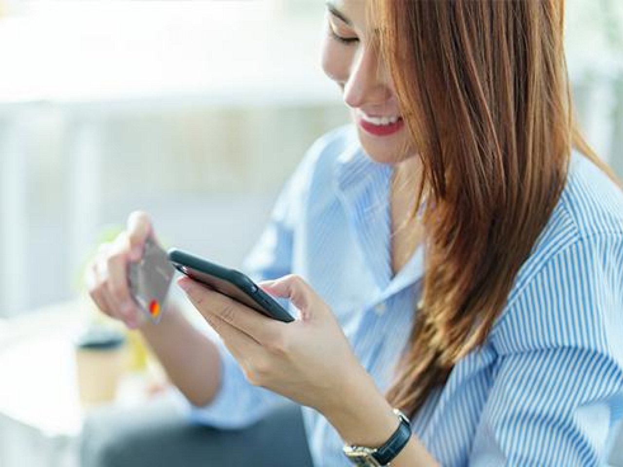 A smiling woman holding her phone and card.