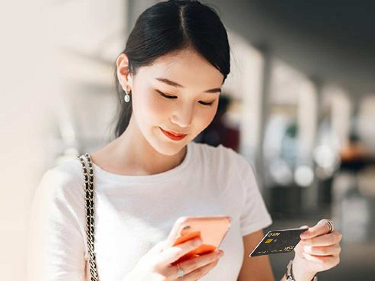 A smiling woman holding her phone and card.