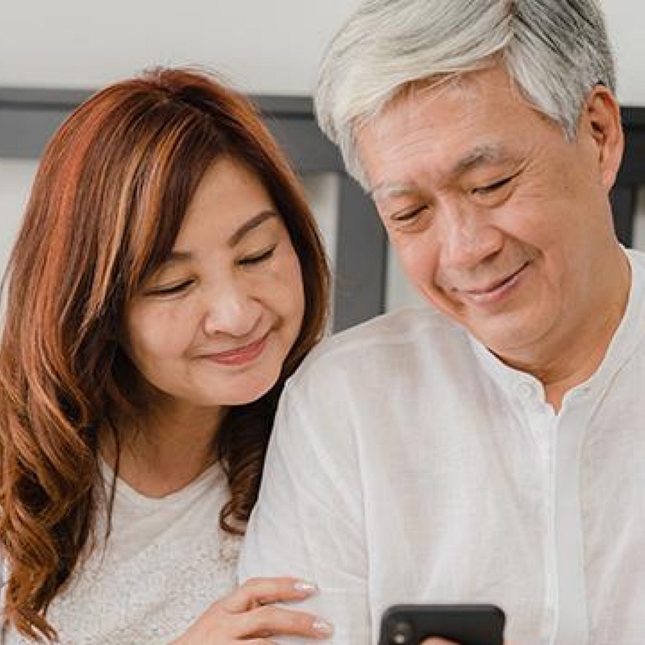 Elderly couple smiling while looking at a mobile phone.