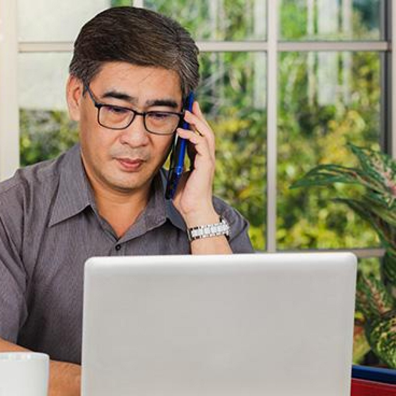 An elderly man on his mobile phone while also working on his laptop.