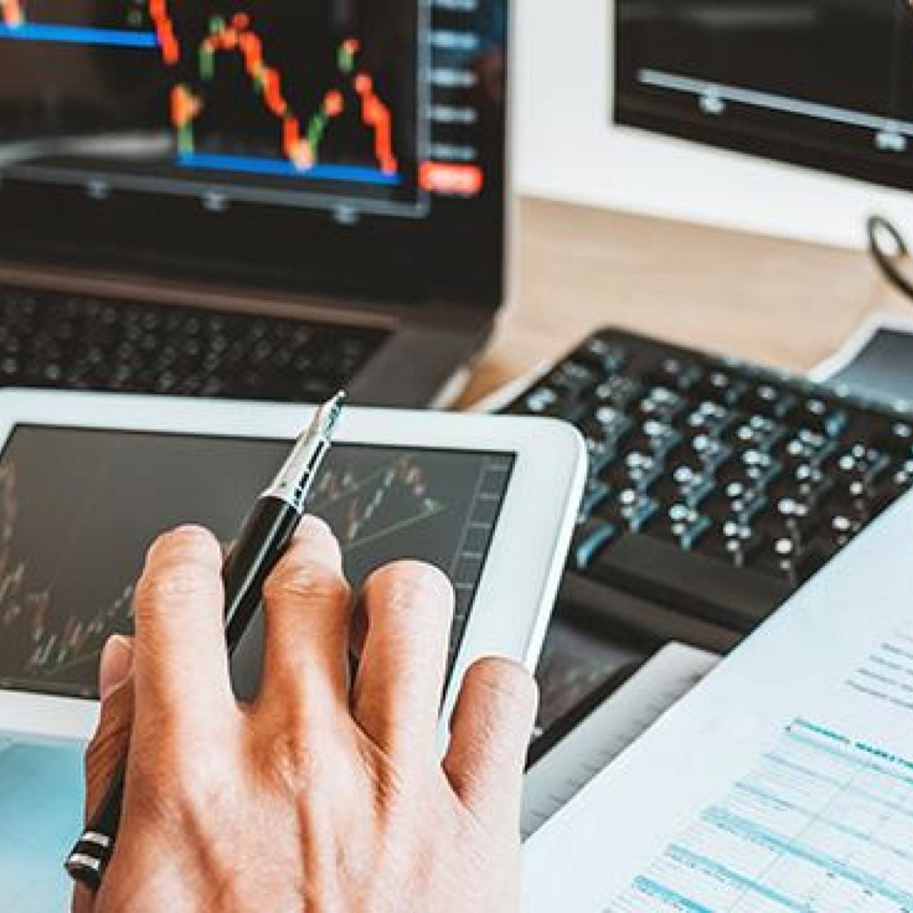 A pair of hands holding a mobile phone and pen with a graph displaying on the phone screen.