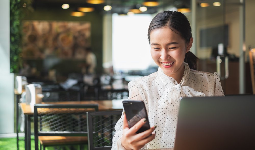 A smiling woman talking over the phone while using her laptop.