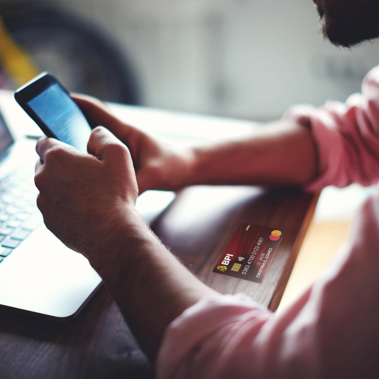 A man holding a phone while in front of his laptop.