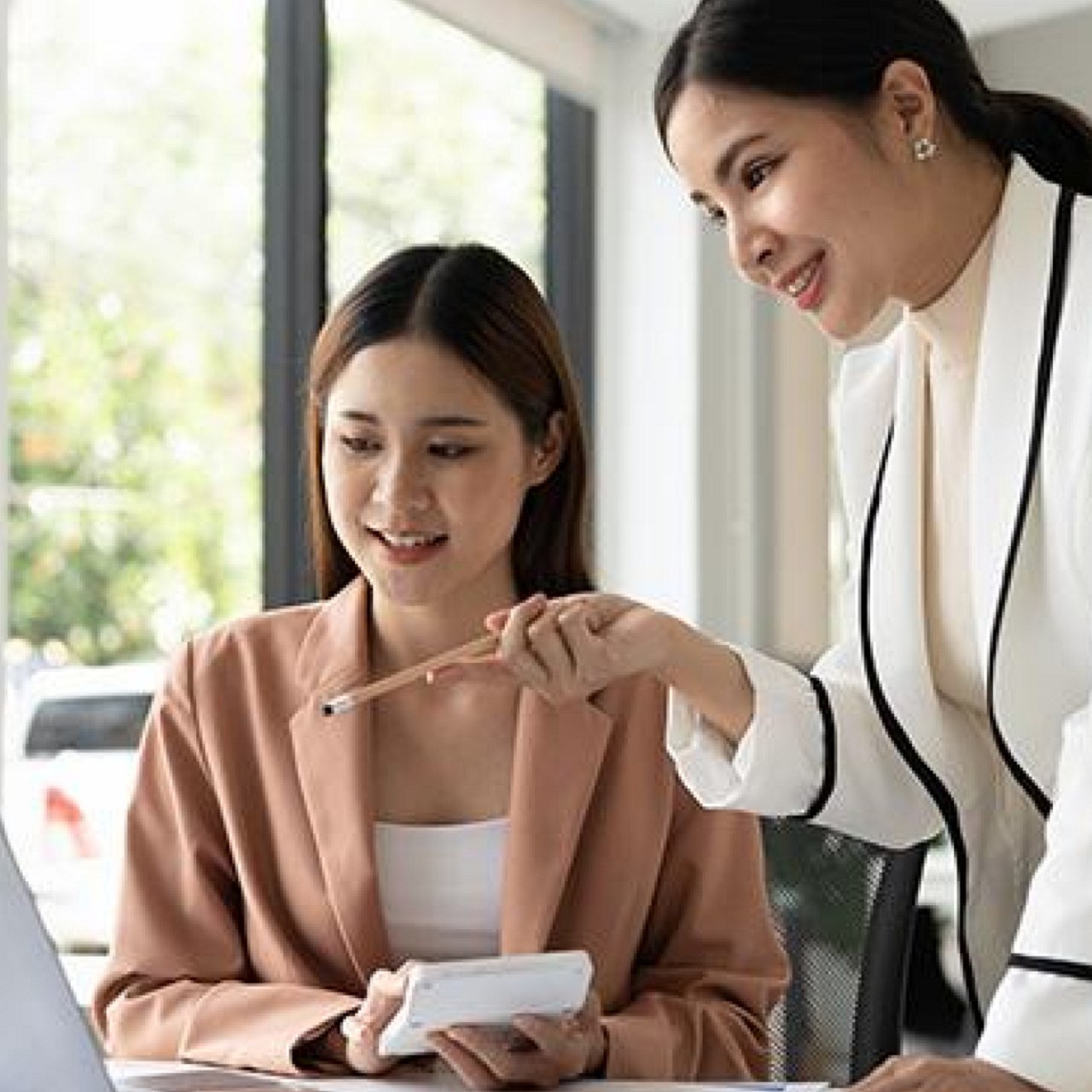 A woman talking to her colleague while looking at a laptop.