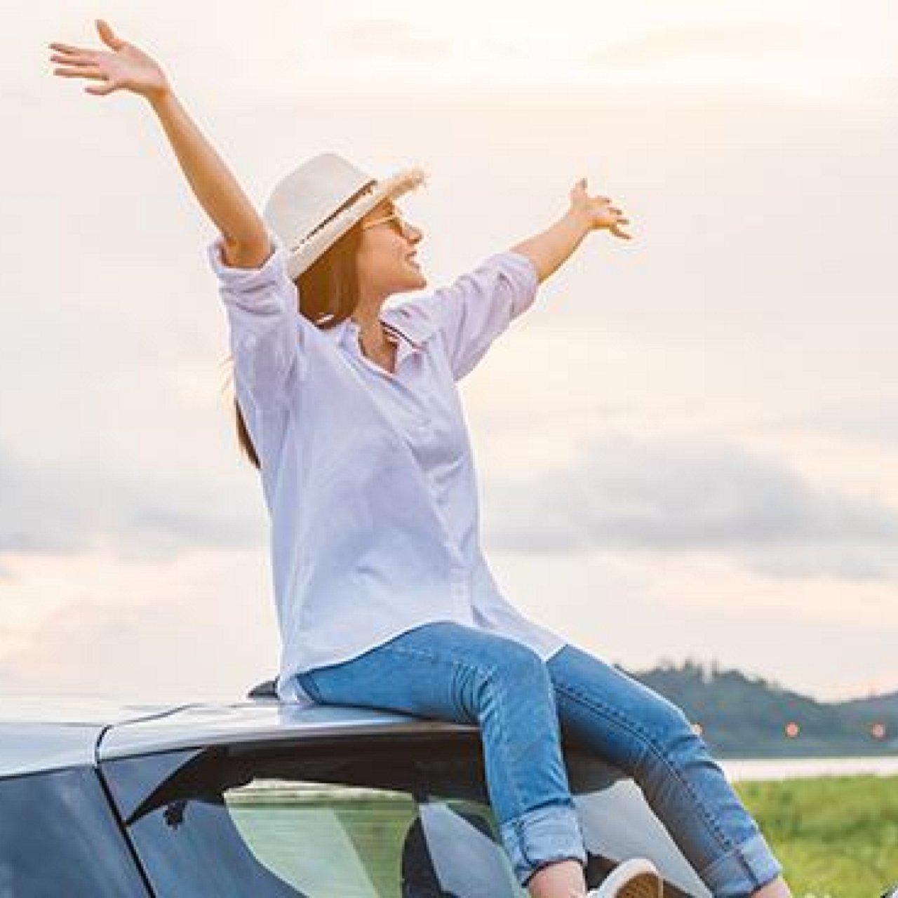 A woman seated on top of her car, enjoying the scenery with hands outstretched