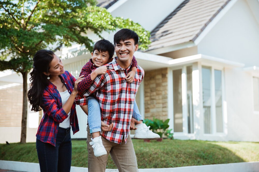 A young boy smiling wide as he enjoys quality time with his parents ouside their new house. 