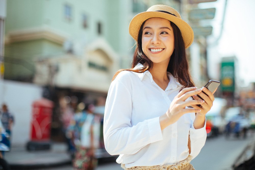A woman smiling while holding her sunglasses.