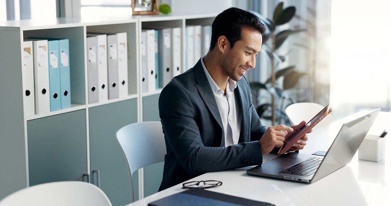 Happy business man, laptop and tablet for data analytics, stock market and online research for profit, sales or company account. Asian trader, investor or analyst in office on digital tech and comput