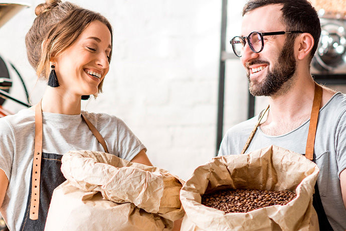 Two barista's holding bags of fresh coffee beans