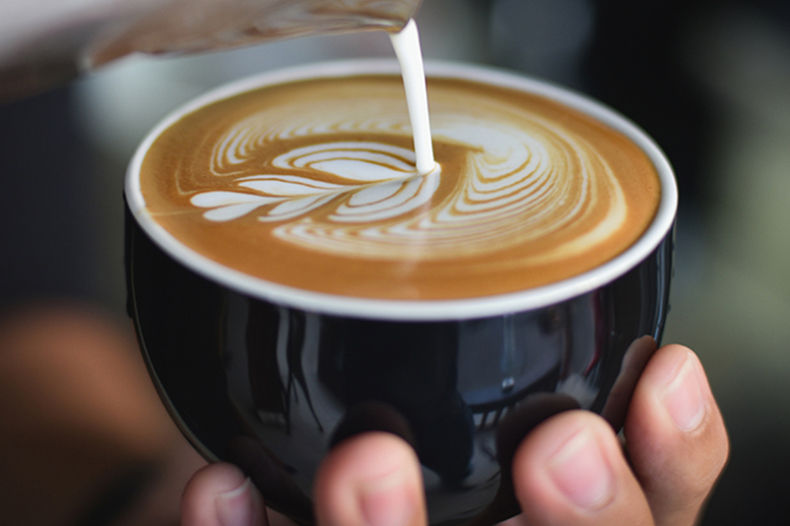 person holding coffee cup creating latte art