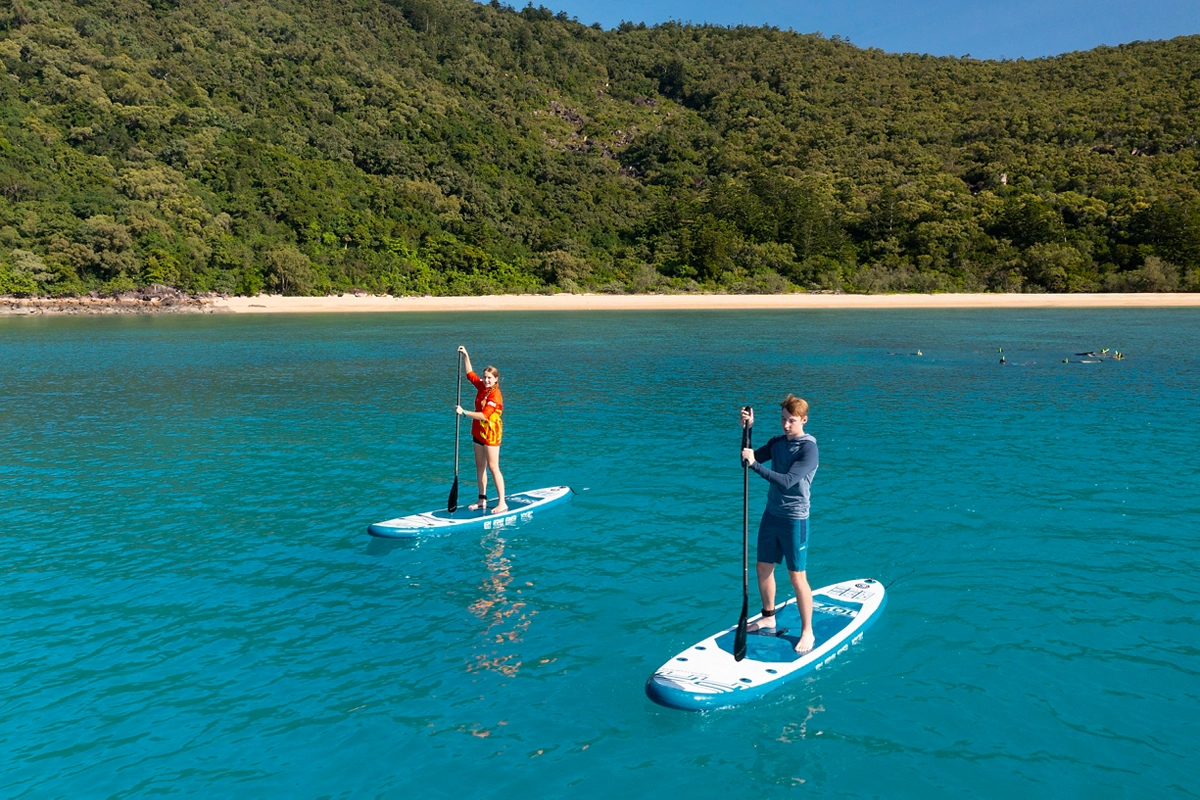 Two people stand-up paddleboard around islands on the Snorkel and Islands Day Tour with Wildcat Mackay Two people stand-up paddleboard around islands on the Snorkel and Islands Day Tour with Wildcat Mackay