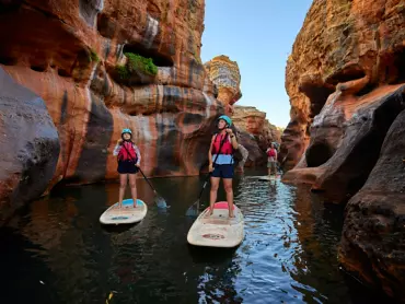 Three people on a stand up paddle boarding tour through Cobbold Gorge 