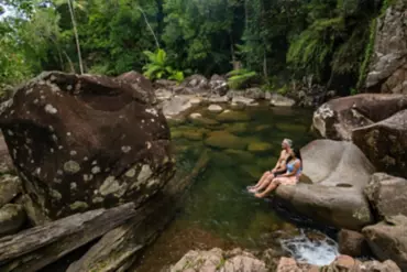 Couple sitting on a boulder looking out over a rock pool at Finch Hatton Gorge