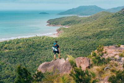 Hiker stands on rocky clifftop overlooking coastline and surrounding islands
