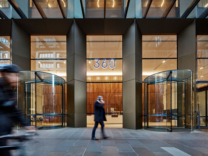 Exterior image of 360 Collins office lobby pedestrian entrance with glass facade and revolving doors 