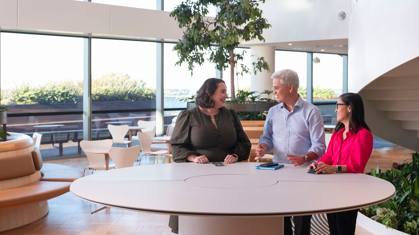 Three people engaged in conversation while standing at a table in an office