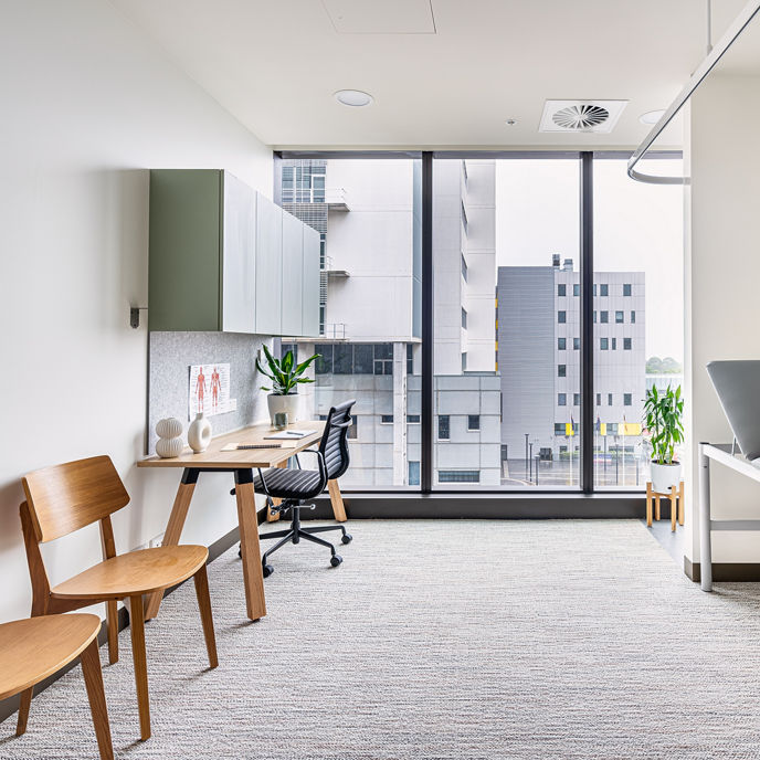 A medical suite at North Shore Health Hub with two chairs, a desk and an exam table 