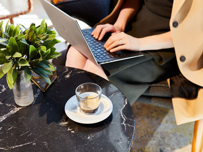 A cup of coffee next to a woman typing on a laptop 