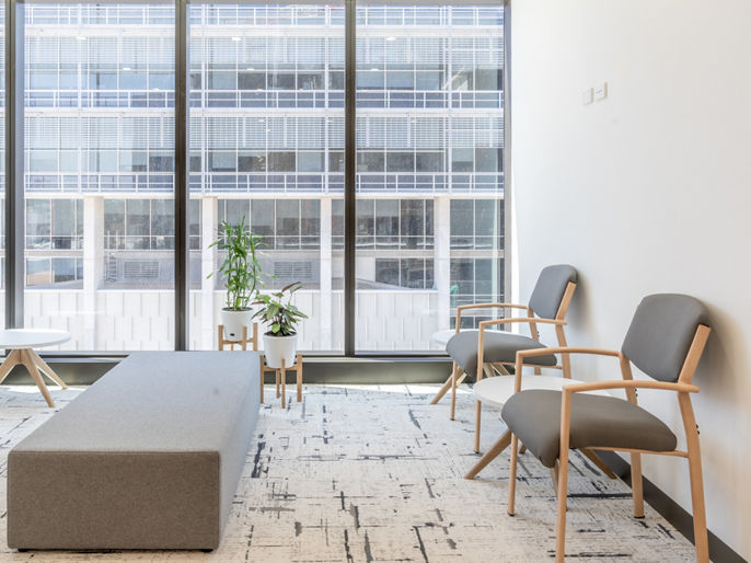 A suite at North Shore Health Hub, with two grey chairs and a bench, and a view of a building from the window 