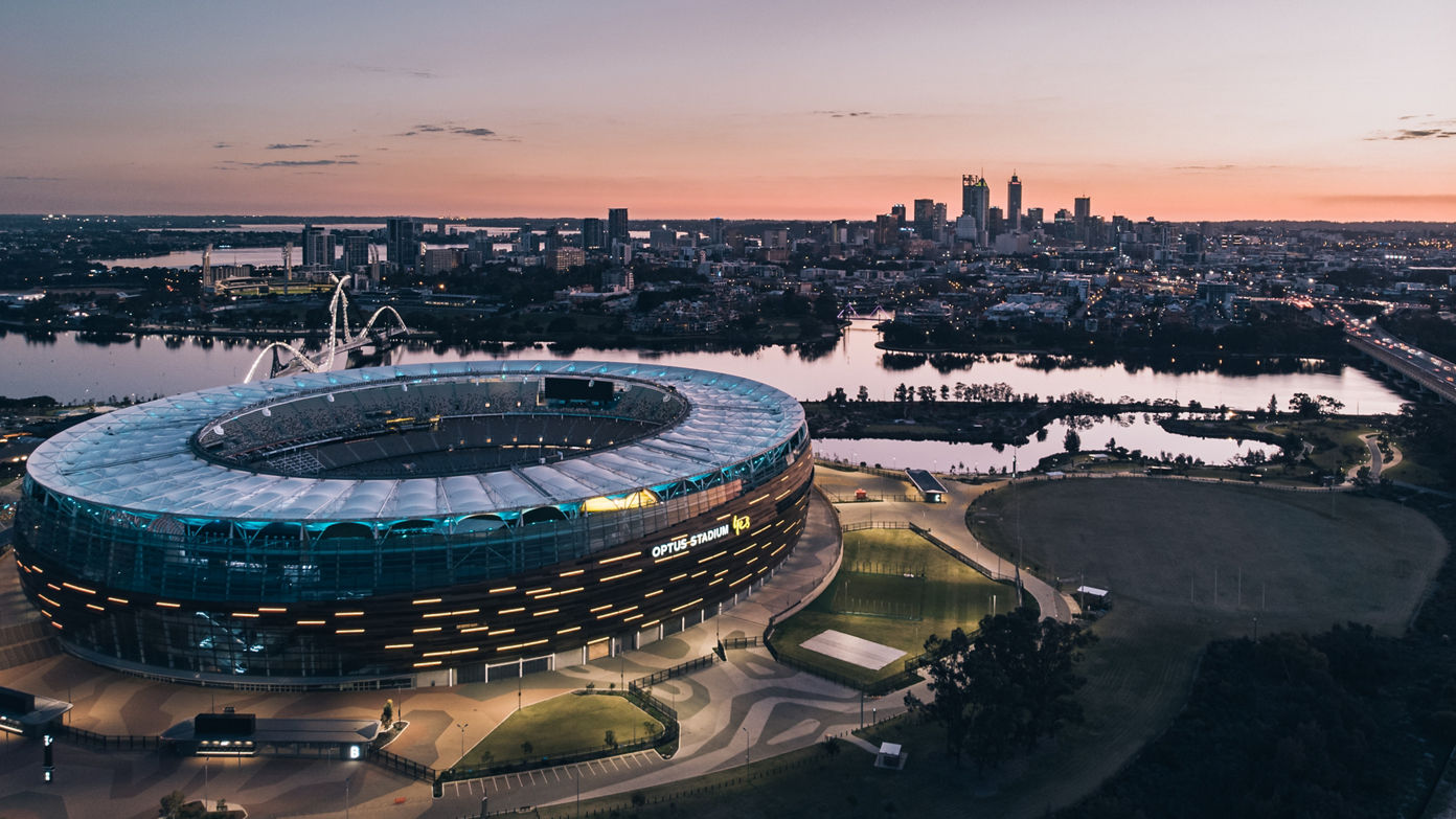 Optus Stadium with Perth and a lilac sky behind it