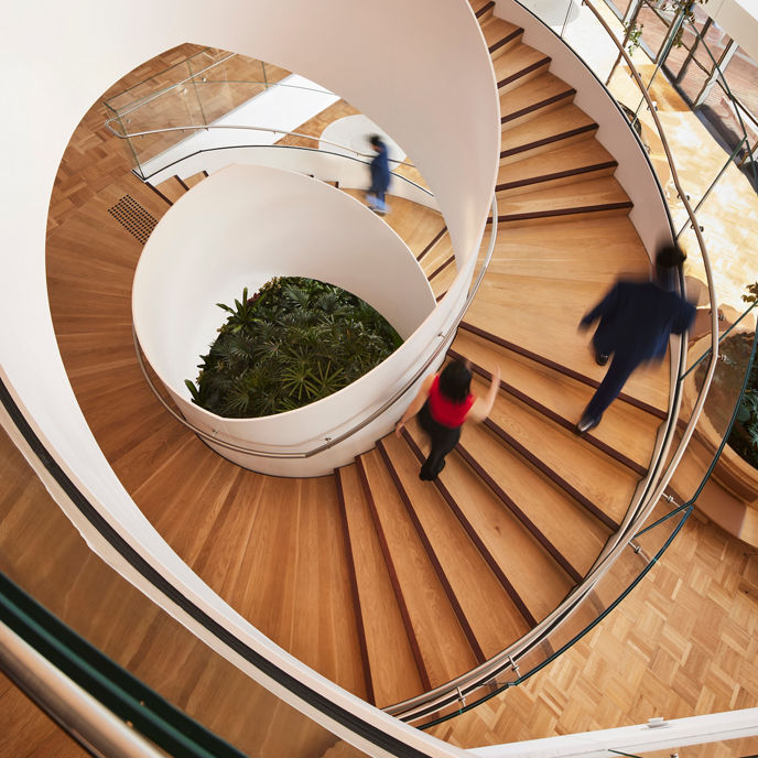 An office space with two people walking up a spiral staircase 