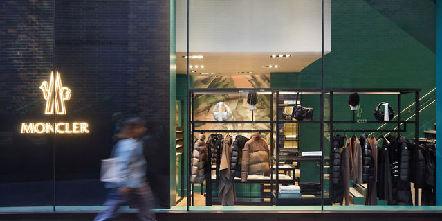A blurred person walking in front of a Moncler storefront 