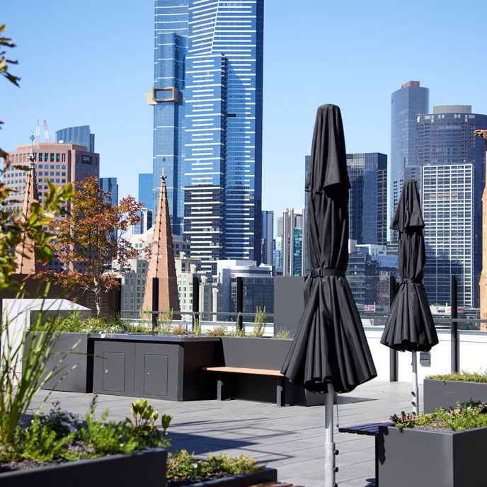 Exterior image of 189 Flinders Lane rooftop terrace with plants, barbeques and umbrellas, overlooking Melbourne skyline