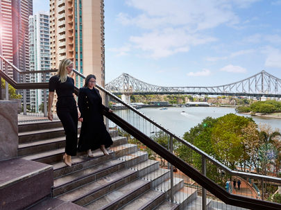 Two people walking down the stairs with Brisbane River in the background