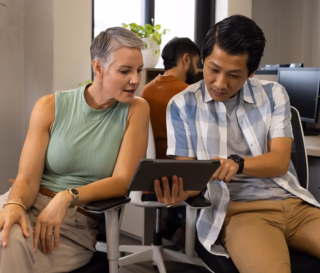 Collaborating Diverse coworkers reviewing tablet in open-plan office, with chairs and plants