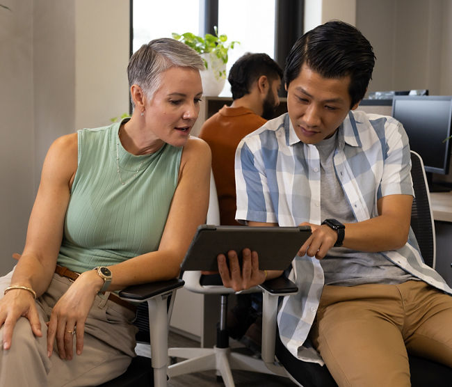 Collaborating Diverse coworkers reviewing tablet in open-plan office, with chairs and plants