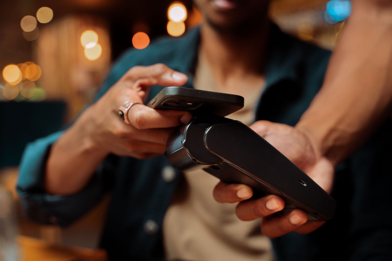 African American customer paying with cellular device and card machine at restaurant. High quality photo