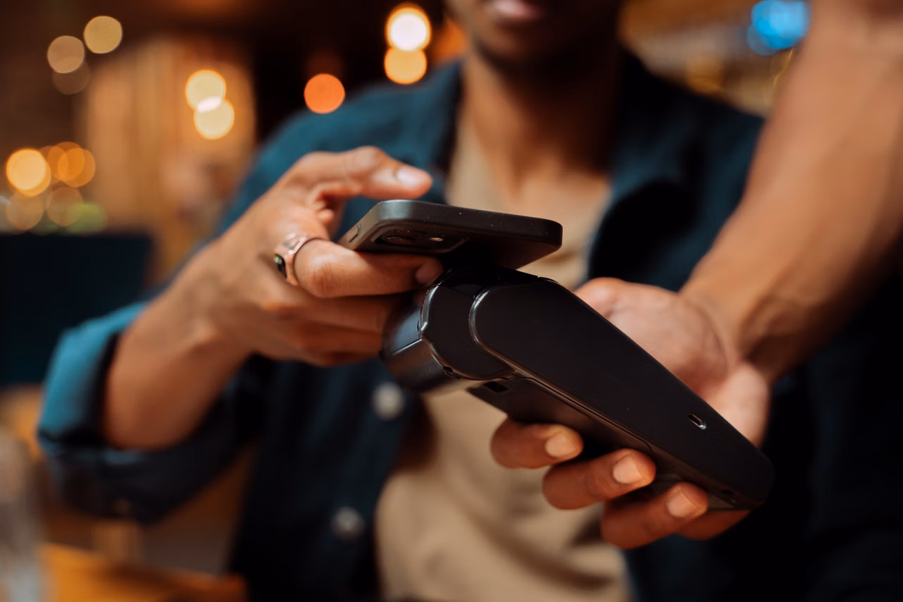 African American customer paying with cellular device and card machine at restaurant. High quality photo
