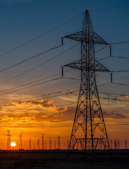 The silhouette of a power grid with high-voltage electricity towers stretching across the landscape during a vibrant sunset