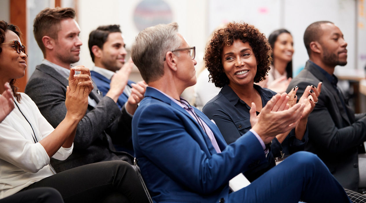 Group Of Businessmen And Businesswomen Applauding Presentation At Conference