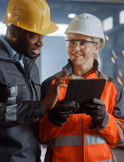 Two Heavy Industry Engineers Stand in Steel Metal Manufacturing Factory, Use Digital Tablet Computer and Have a Discussion. Black African American Industrial Specialist Talk to Female Technician.