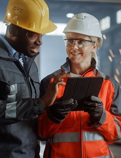 Two Heavy Industry Engineers Stand in Steel Metal Manufacturing Factory, Use Digital Tablet Computer and Have a Discussion. Black African American Industrial Specialist Talk to Female Technician.