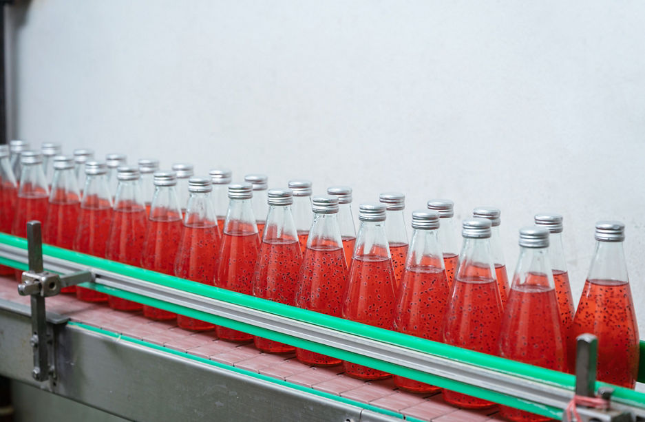 Glass bottled red juice on steel conveyor of production line in beverage processing plant