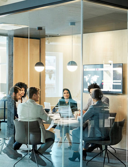 Business colleagues sitting at conference table seen through glass wall. Multi-ethnic coworkers are discussing in board room at office. They are planning strategy.