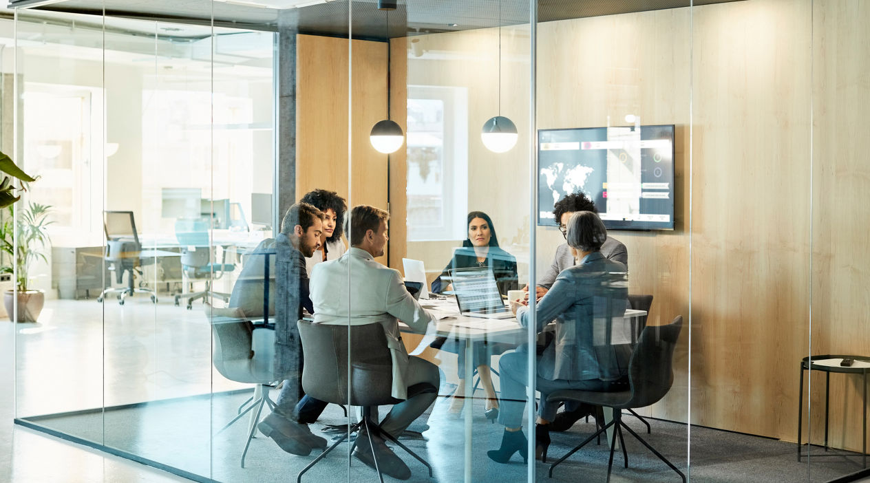Business colleagues sitting at conference table seen through glass wall. Multi-ethnic coworkers are discussing in board room at office. They are planning strategy.