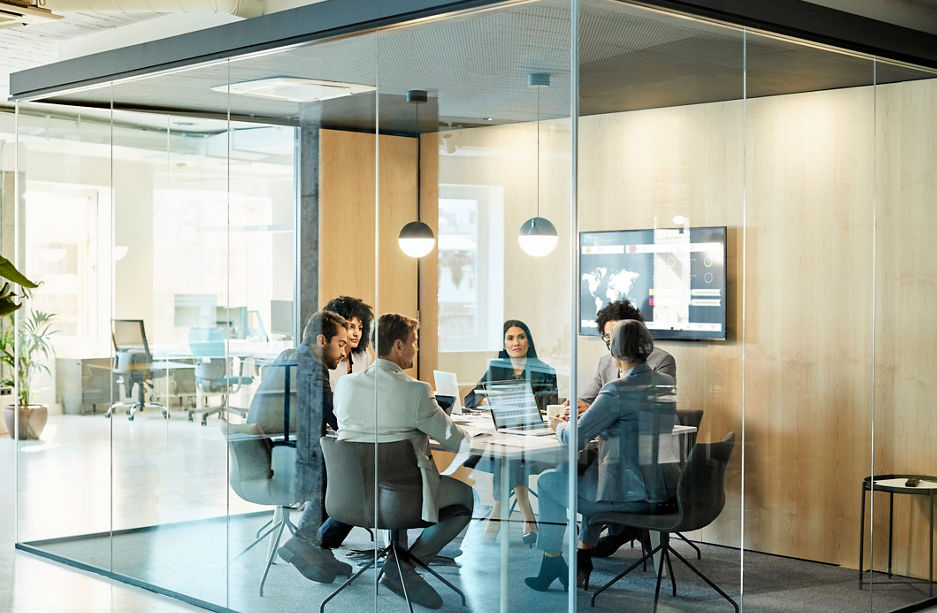 Business colleagues sitting at conference table seen through glass wall. Multi-ethnic coworkers are discussing in board room at office. They are planning strategy.